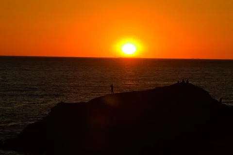Dramatic ocean sunset with dark cliff silhouette and one person watching horizon Stock-Fotos