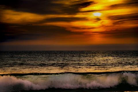 Dramatic ocean sunset with fiery clouds and crashing wave Photos