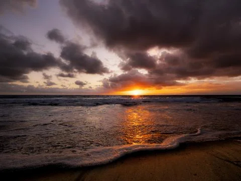 Dramatic ocean sunset with fiery orange sun breaking through dark clouds Fotos de archivo