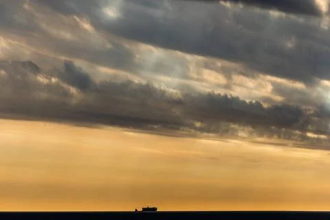A dramatic ocean sunset with a lone ship and cloudy sky, creating a serene... Stock Photos