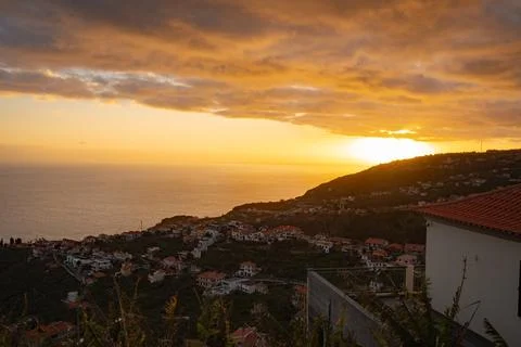Dramatic ocean sunset over a coastal town nestled on lush green hills, vibr.. Stock Photos