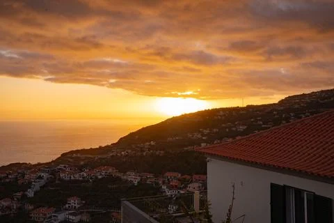 Dramatic ocean sunset over a hillside village, casting warm glow on homes a.. Stock Photos
