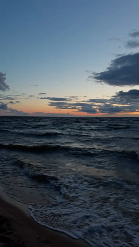 Dramatic ocean sunset with rolling waves, glowing horizon, and moody clouds over Stock Footage 345455867