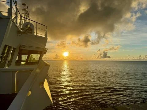 Dramatic ocean sunset viewed from ship deck with golden sky and calm sea horizon Foto stock
