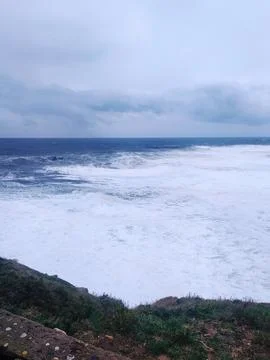 Dramatic ocean view with powerful waves crashing against the shore under a mo Stock Photos
