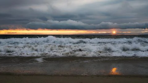 Dramatic ocean waves crash on the shore during a vibrant sunset with stormy.. Photos