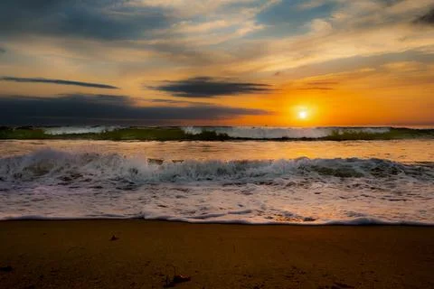 Dramatic ocean waves crash on the shore during a vibrant sunset Fotos de archivo