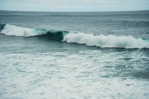 Dramatic ocean waves crest and break creating white foam on deep blue-green w Stock Photos