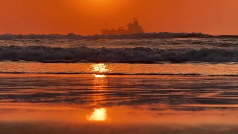 Dramatic ocean waves on sandy beach at sunset with large ship silhouette Stock Footage 342219134
