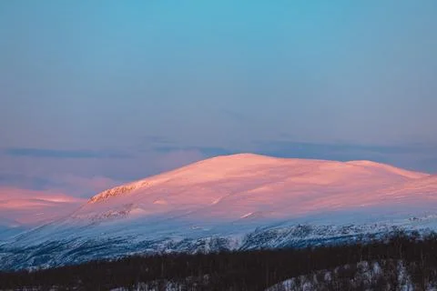 Dramatic orange and pink sunset clouds spread across a blue Arctic sky in A.. Stock Photos