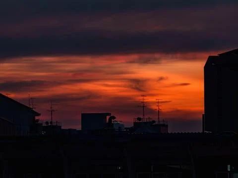 Dramatic orange and red sunset sky over city rooftops silhouette with TV an.. Stock Photos