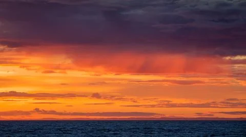 Dramatic orange cloudscape over deep blue water at sunset Stock Photos