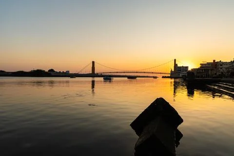 Dramatic orange sky over river with bridge silhouette and calm water 库存照片