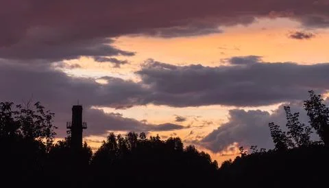 Dramatic orange sunset behind dark clouds and tree silhouettes, atmospheric Stock Photos