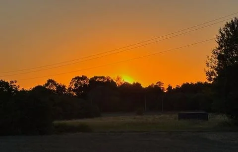 Dramatic orange sunset behind trees and rural landscape. Stock Photos