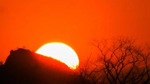 Dramatic orange sunset or sunrise. Bright sun behind mountain, silhouetted .. Stock Photos