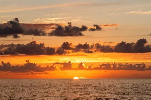 Dramatic orange sunset paints the sky above a calm sea with scattered clouds Stock Photos