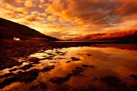 Dramatic orange sunset shine on a Scottish loch with mountains reflected Stock Photos