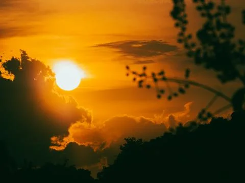 Dramatic orange sunset sky with a bright glowing sun partly behind dark sil.. Stock Photos