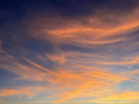 Dramatic orange sunset sky with cirrus clouds and airplane contrails Stock Photos