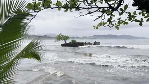 Dramatic overcast coastal scene frames weathered shipwreck amid crashing waves Stock Footage 337948624