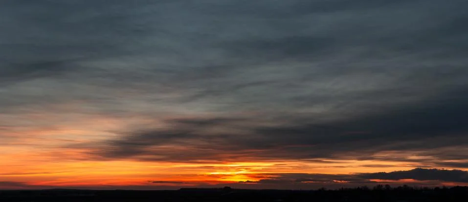 Dramatic panorama of bright saturated sunset with many dark clouds Stock Photos