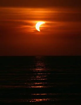 Dramatic Partial Solar Eclipse and Vibrant Red Sunset Over Sea Stock Photos