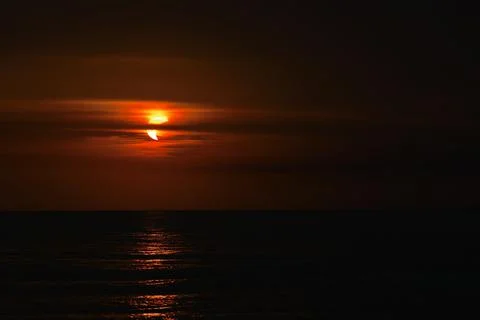 Dramatic Partial Solar Eclipse and Vibrant Red Sunset Over Sea Stock Photos