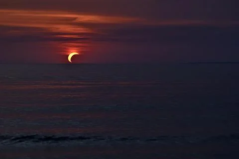 Dramatic Partial Solar Eclipse and Vibrant Red Sunset Over Sea Stock Photos