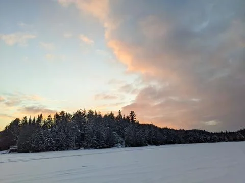 Dramatic Pastel Sunset Clouds Over Frozen Snow Covered Lake and Winter Forest Foto stock