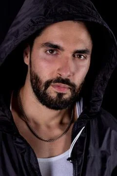 Dramatic portrait of handsome bearded man wearing dark hood on a black backgr Stock Photos