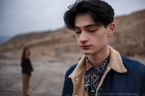 Dramatic portrait of a young brunette guy in cloudy weather. somewhere behind Stock Photos