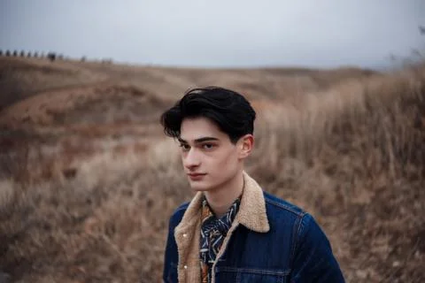 Dramatic portrait of a young brunette guy in cloudy weather against the backg Stock Photos