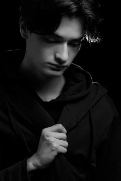 Dramatic portrait of a young guy in a black hoodie on a black background. bla Stock Photos