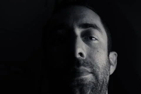 Dramatic portrait of a young man half expressionless face in deep shadow look Stock Photos