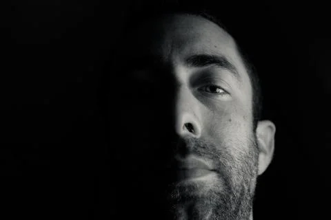Dramatic portrait of a young man half expressionless face in deep shadow look Stock Photos