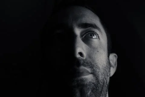 Dramatic portrait of a young man half expressionless face in deep shadow look Stock Photos