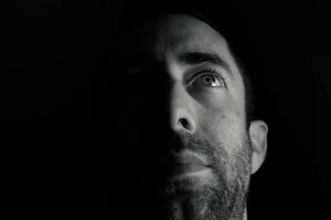 Dramatic portrait of a young man half expressionless face in deep shadow look Stock Photos