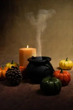 Dramatic potion making cauldron smoking with orange candle and small pumpkins Stock Photos
