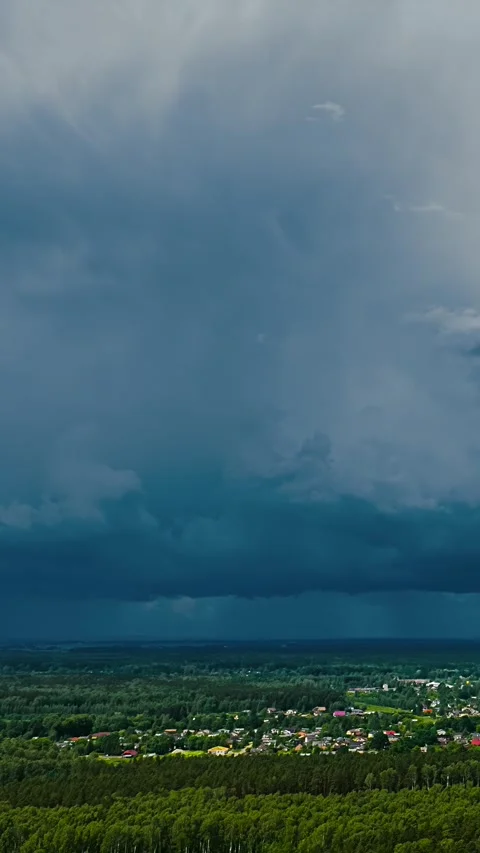 Dramatic rain clouds gather over a small village surrounded by lush green f.. Stock Footage 337716060