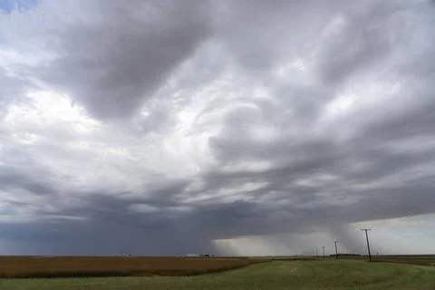 Dramatic rain shower falling over farmland under storm clouds Dark storm c... Stock Photos