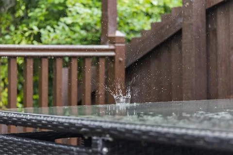 Dramatic raindrop creates a crown-like splash on a wet glass patio table Stock Photos