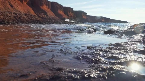 Dramatic red clay cliffs overlook a rocky ocean shoreline landscape. Stock Footage 337408771