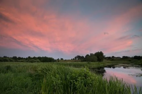 Dramatic red evening clouds over the meadow and the river. 写真素材