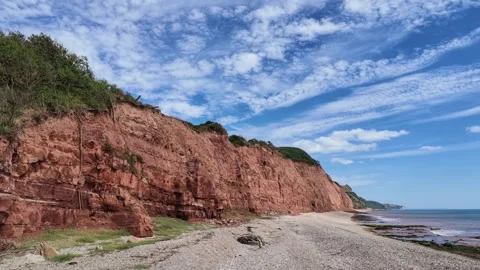 Dramatic red sandstone cliffs meet the ocean under a vast blue sky with cloud Stock Footage 343530687