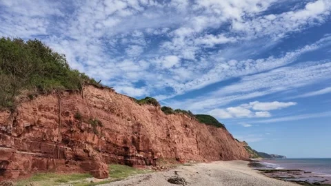 Dramatic red sandstone cliffs meet the ocean under a vast blue sky with cloud Stock Footage 343531123