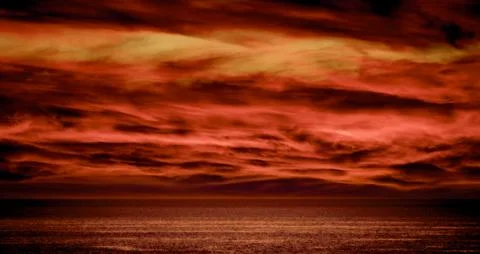 Dramatic red sky with fiery clouds over a calm ocean horizon 스톡 사진