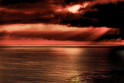 Dramatic red sky over the ocean with dark clouds and reflections 스톡 사진