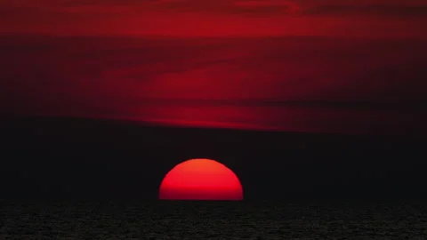 Dramatic red sun setting over dark ocean horizon at dusk Stock Footage 345681603
