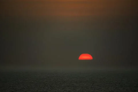 Dramatic red sun setting over a dark, rippling ocean horizon Photos